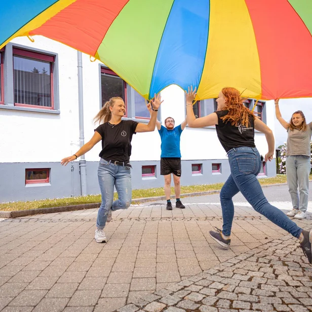 Ergotherapie-Schülerinnen laufen gemeinsam unter einem Schwungtuch. Ergotherapie-Schülerinnen laufen gemeinsam unter einem Schwungtuch.