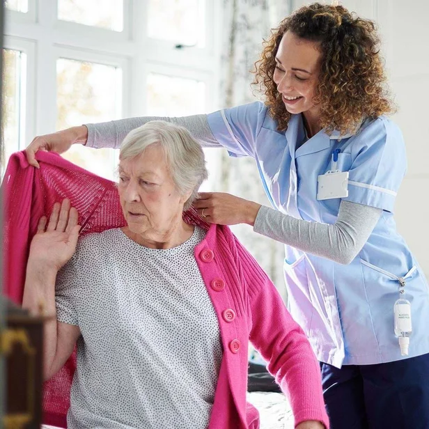 Pflegefachkraft hilft einer Patientin beim Anziehen.