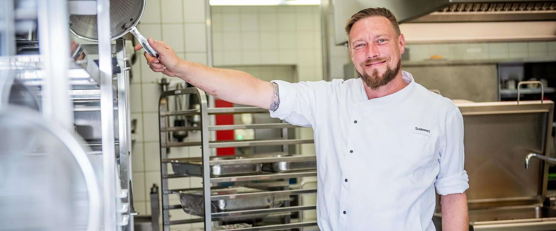 Eric Schimmel steht in der Küche und lächelt in die Kamera.