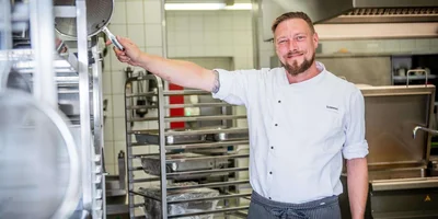 Eric Schimmel steht in der Küche und lächelt in die Kamera.