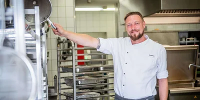 Eric Schimmel steht in der Küche und lächelt in die Kamera.