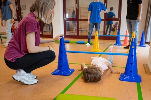 Ergotherapie-Schülerin begleitet ein Kleinkind bei Bewegungsübungen. Ergotherapie-Schülerin begleitet ein Kleinkind bei Bewegungsübungen.