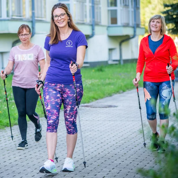 Bewegungstherapeutin leitet eine Nordic-Walking-Gruppe im Freien.