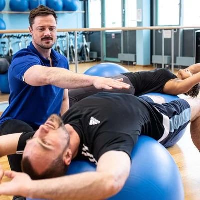 Physiotherapeut begleitet einen Patienten bei Übungen mit dem Pezziball.