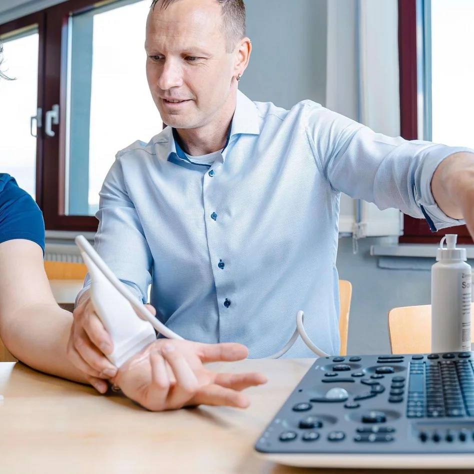 Lehrer erklärt einem Physiotherapie-Schüler eine Ultraschalluntersuchung am Handgelenk. Lehrer erklärt einem Physiotherapie-Schüler eine Ultraschalluntersuchung am Handgelenk.