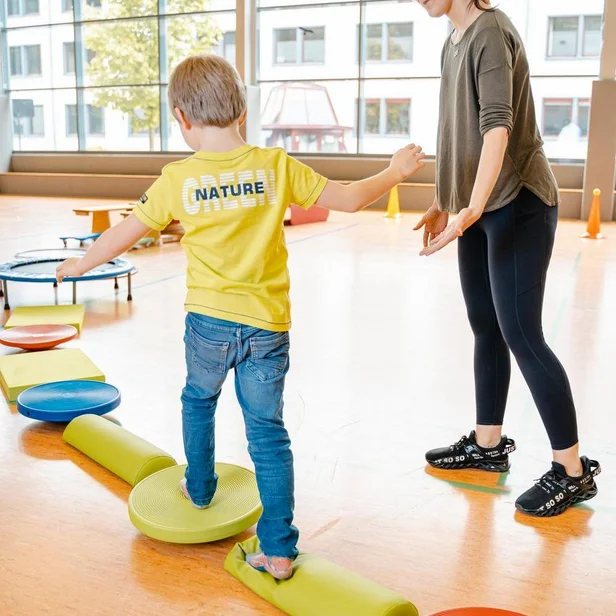 Ergotherapie-Schülerin begleitet ein Kleinkind bei Balanceübungen auf Balanciersteinen. Ergotherapie-Schülerin begleitet ein Kleinkind bei Balanceübungen auf Balanciersteinen.