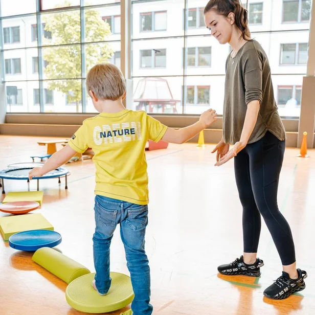 Ergotherapie-Schülerin begleitet ein Kleinkind bei Balanceübungen auf Balanciersteinen. Ergotherapie-Schülerin begleitet ein Kleinkind bei Balanceübungen auf Balanciersteinen.
