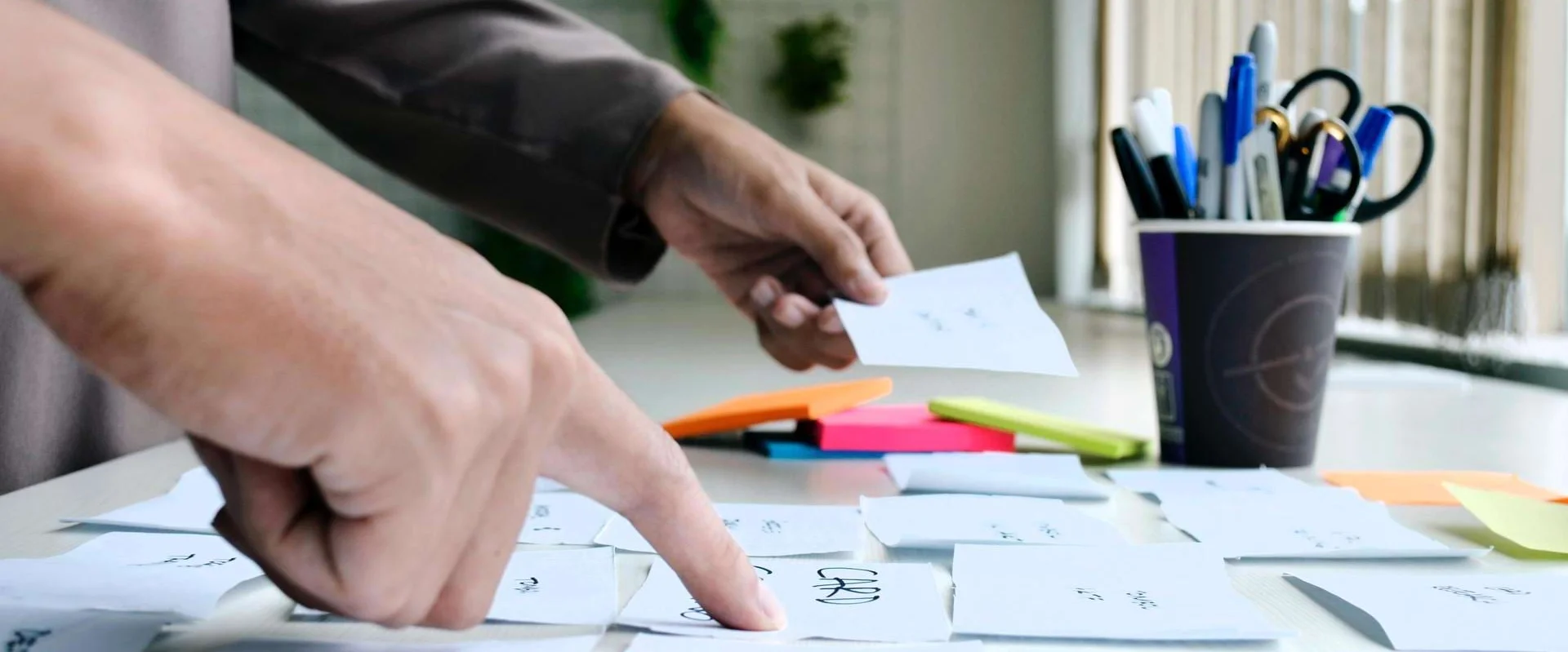 Besprechungstisch bei Fortbildung mit Post its und Hände, die darauf zeigen.