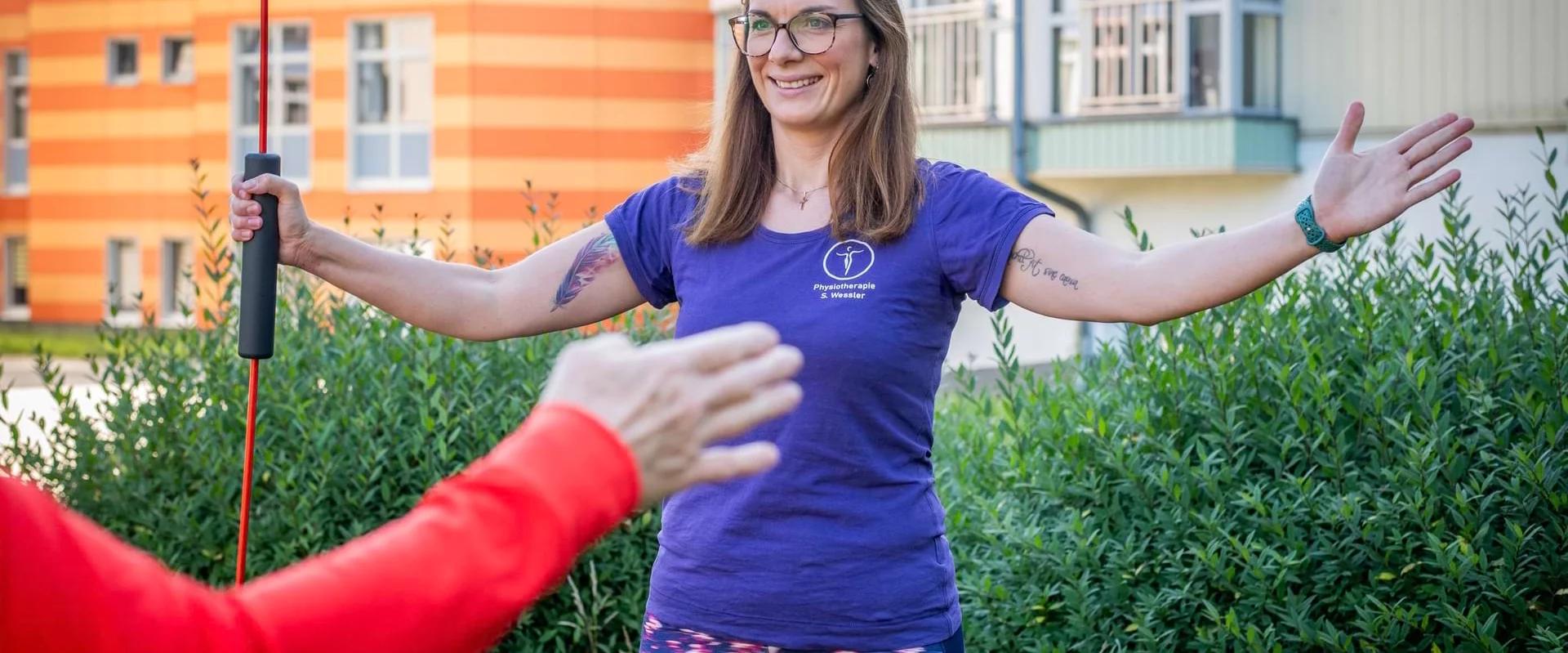 Physiotherapeutin Sarah Wessler zeigt eine aktive Übung zur Schulterbeweglichkeit.