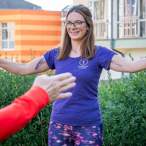 Physiotherapeutin Sarah Wessler zeigt eine aktive Übung zur Schulterbeweglichkeit.