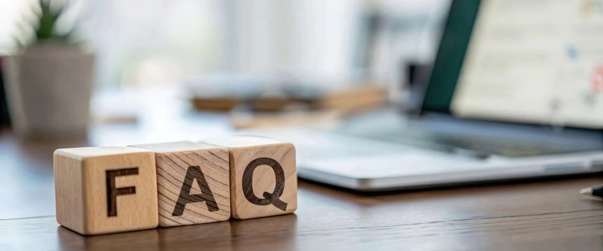 Holzklötzchen mit dem Schriftzug „FAQ“ stehen auf einem Schreibtisch. Holzklötzchen mit dem Schriftzug „FAQ“ stehen auf einem Schreibtisch.