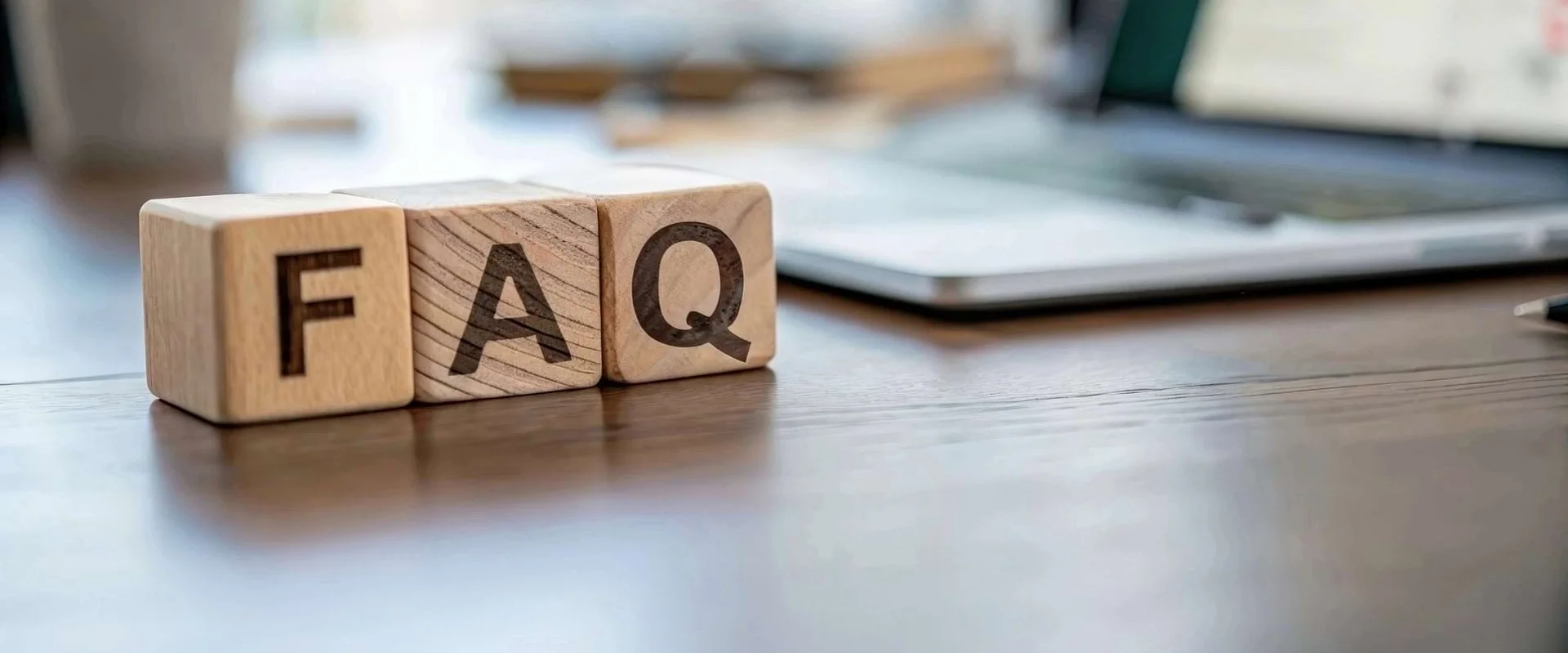 Holzklötzchen mit dem Schriftzug „FAQ“ stehen auf einem Schreibtisch.