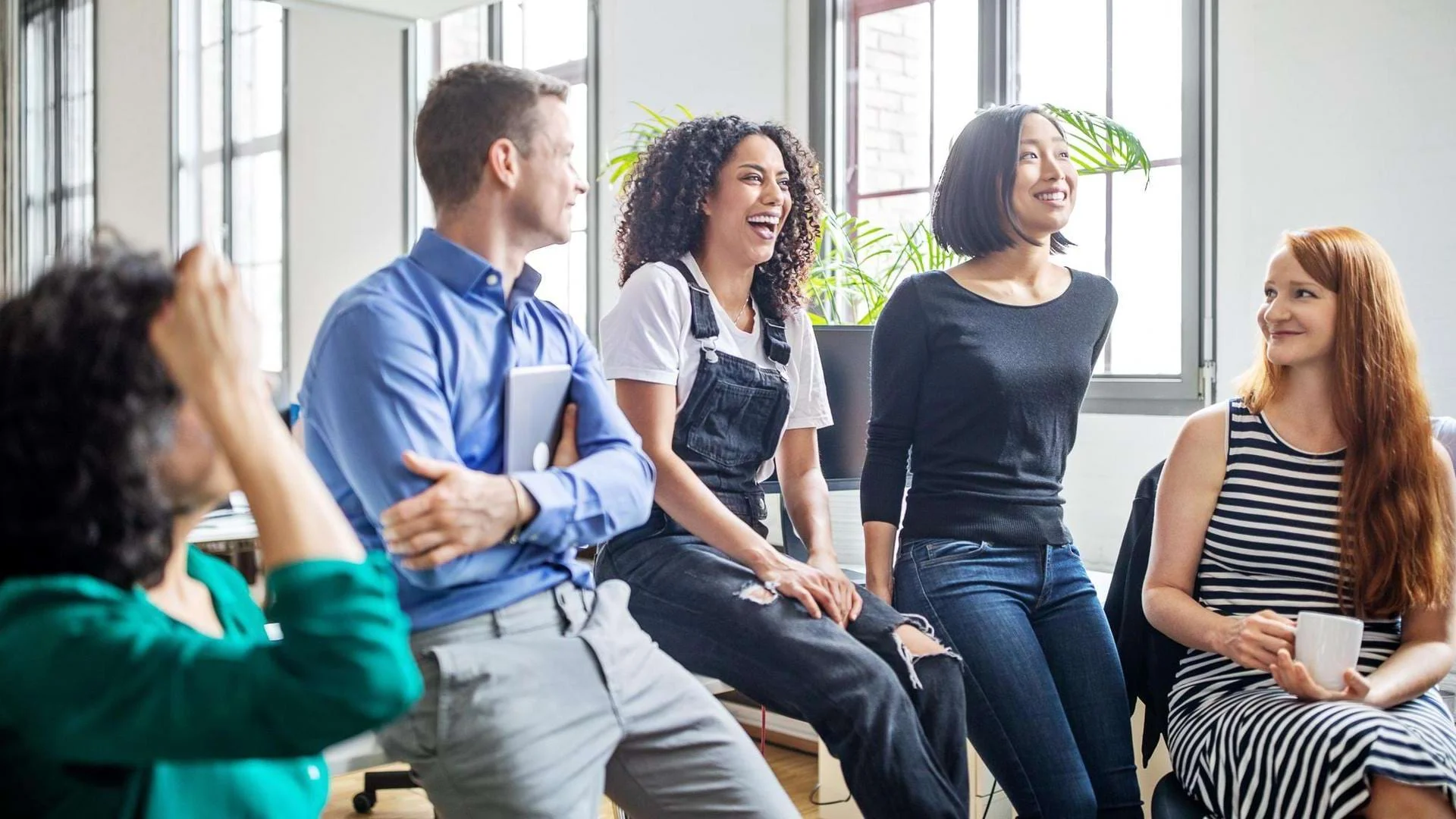 Teilnehmer der Fortbildung Sozialdienst sitzen auf Tisch und lachen., Bild öffnen