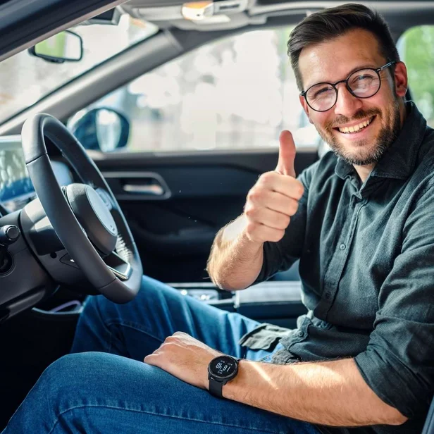 Mitarbeiter im Fahrdienst sitzt am Steuer eines Autos und zeigt lächelnd einen Daumen nach oben. Mitarbeiter im Fahrdienst sitzt am Steuer eines Autos und zeigt lächelnd einen Daumen nach oben.