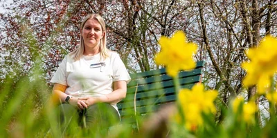 Anne Tauscher, Gesundheits- und Krankenpflegerin, sitzt draußen auf einer grünen Bank. Anne Tauscher, Gesundheits- und Krankenpflegerin, sitzt draußen auf einer grünen Bank.