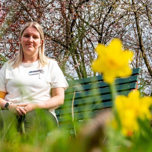 Anne Tauscher, Gesundheits- und Krankenpflegerin, sitzt draußen auf einer grünen Bank.