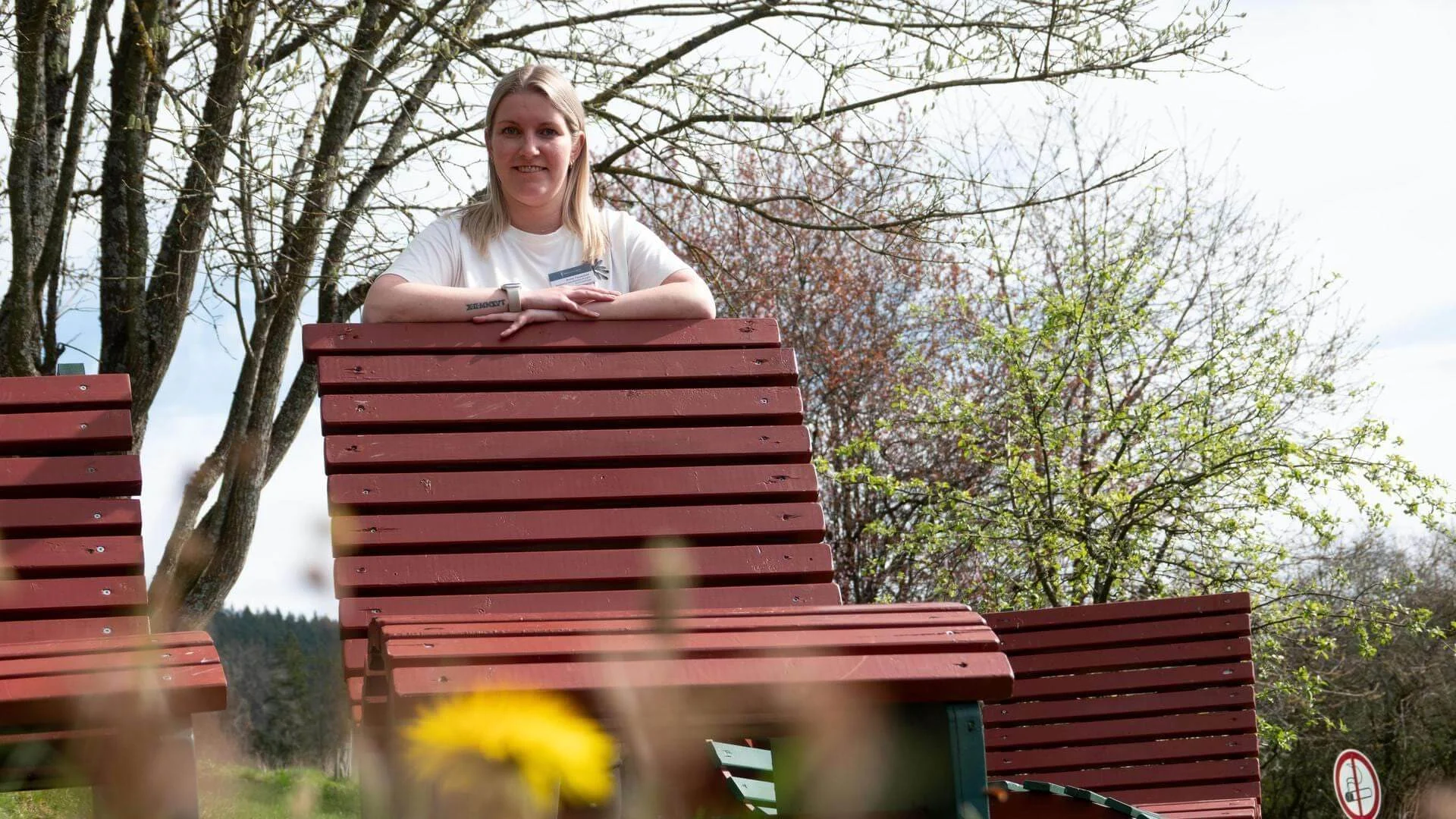 Anne Tauscher, Mitglied des Pflegedienstes, steht hinter einer Bank im Garten der Klinik. Anne Tauscher, Mitglied des Pflegedienstes, steht hinter einer Bank im Garten der Klinik.