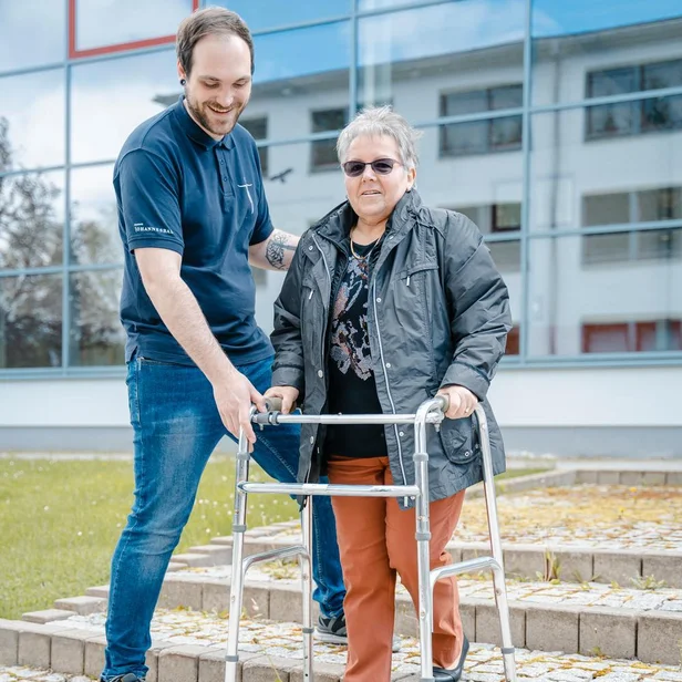 Ergotherapie-Schüler unterstützt eine Patientin beim Gehen mit einer Gehhilfe. Ergotherapie-Schüler unterstützt eine Patientin beim Gehen mit einer Gehhilfe.