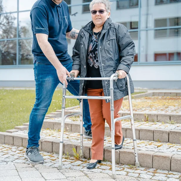 Ergotherapie-Schüler unterstützt eine Patientin beim Gehen mit einer Gehhilfe. Ergotherapie-Schüler unterstützt eine Patientin beim Gehen mit einer Gehhilfe.