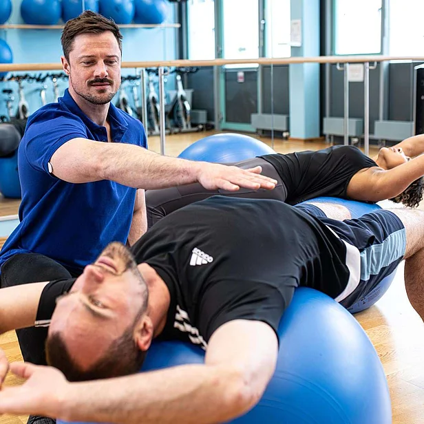 Physiotherapeut begleitet einen Patienten bei Übungen mit dem Pezziball.
