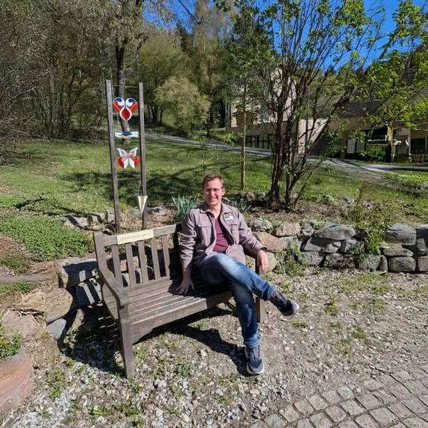 Simon Lössl, Psychologe, sitzt auf einer Bank bei der Johannesbad Fachklinik Furth im Wald