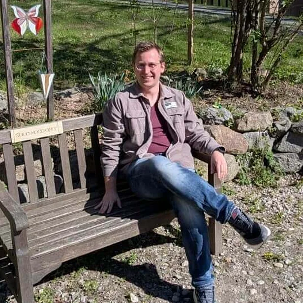 Simon Lössl, Psychologe, sitzt auf einer Bank bei der Johannesbad Fachklinik Furth im Wald Simon Lössl, Psychologe, sitzt auf einer Bank bei der Johannesbad Fachklinik Furth im Wald