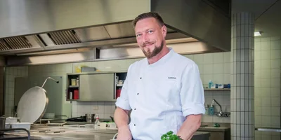 Eric Schimmel steht in der Küche und bereitet frische Zutaten zu. Eric Schimmel steht in der Küche und bereitet frische Zutaten zu.