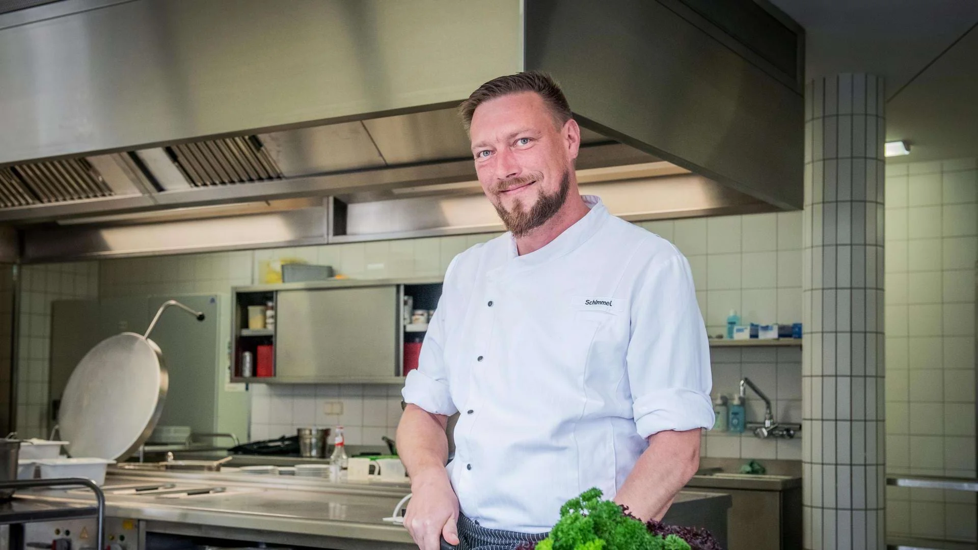 Eric Schimmel steht in der Küche und bereitet frische Zutaten zu. Eric Schimmel steht in der Küche und bereitet frische Zutaten zu.