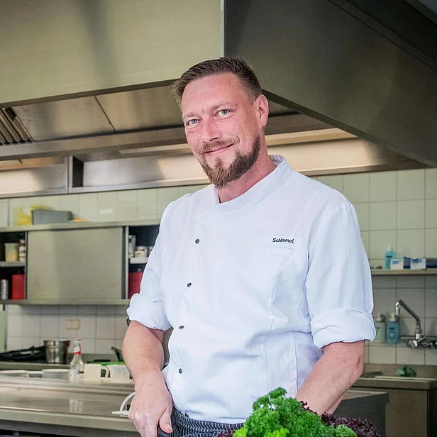 Eric Schimmel steht in der Küche und bereitet frische Zutaten zu. Eric Schimmel steht in der Küche und bereitet frische Zutaten zu.
