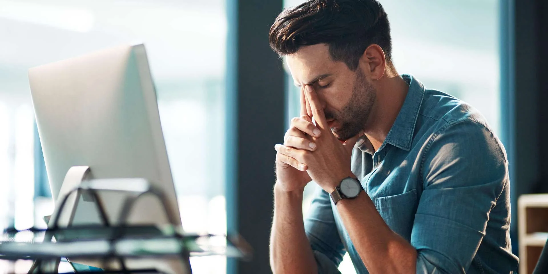 Mitarbeiter sitzt vor Bildschirm und legt nachdenklich Kopf auf die Hände Mitarbeiter sitzt vor Bildschirm und legt nachdenklich Kopf auf die Hände