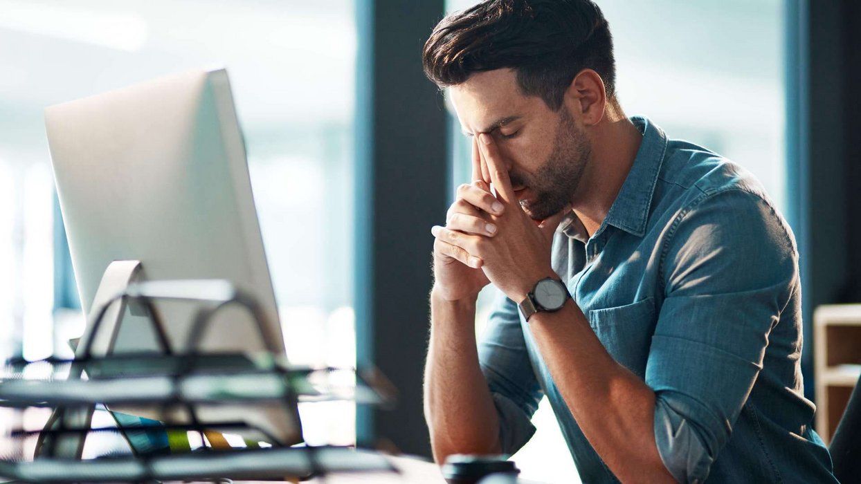 Mitarbeiter sitzt vor Bildschirm und legt nachdenklich Kopf auf die Hände