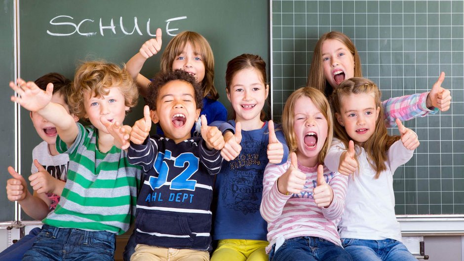 Kinder sitzen vor Tafel und halten Daumen nach oben