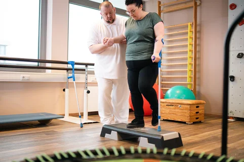 Ergotherapie-Schüler begleitet eine Patientin bei einer Übung am Stepper. Ergotherapie-Schüler begleitet eine Patientin bei einer Übung am Stepper.