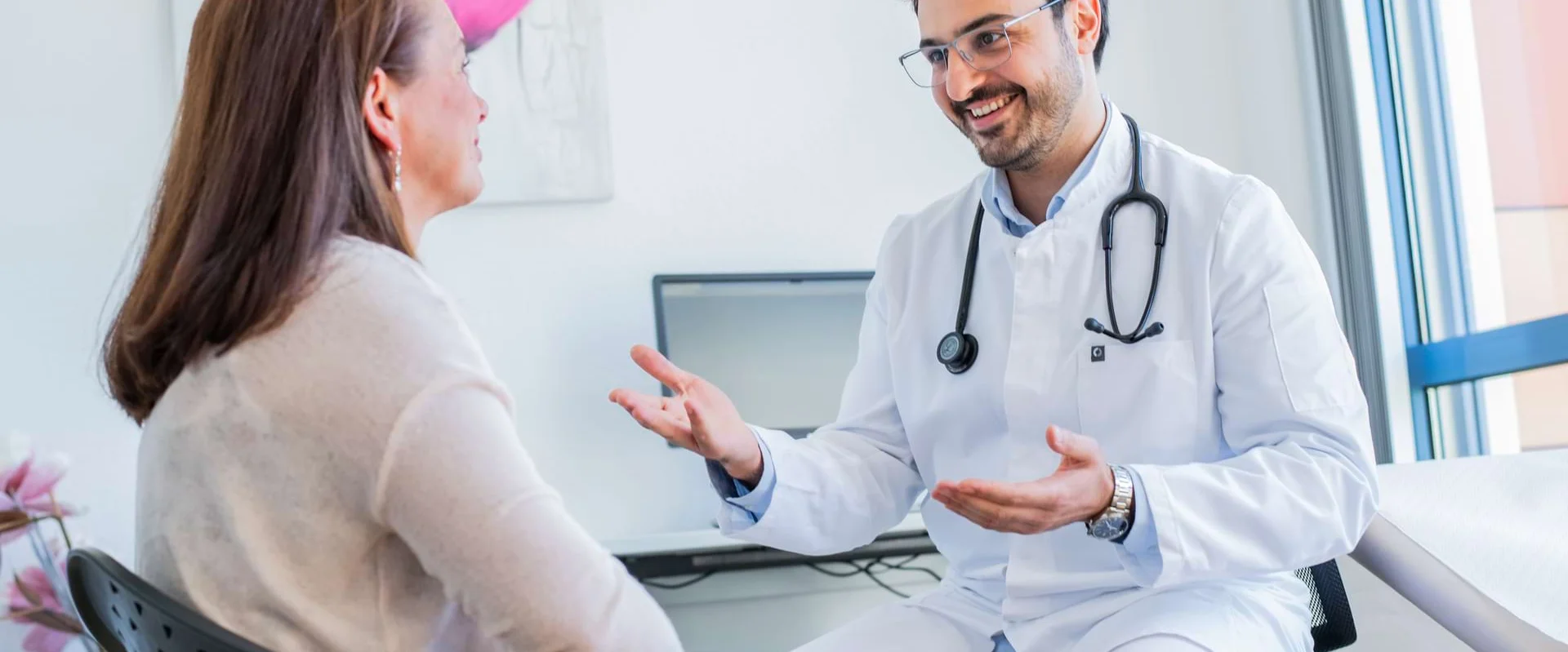 Ein Arzt sitzt im Gespräch mit einer Patientin im Behandlungsraum.