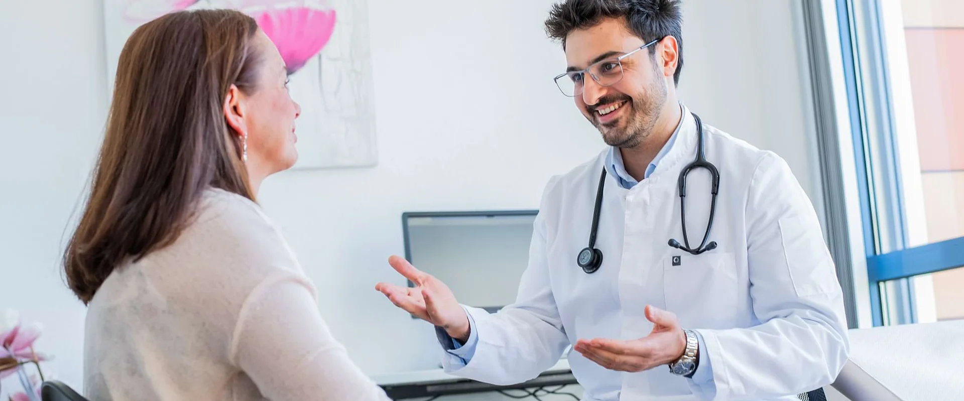 Ein Arzt sitzt im Gespräch mit einer Patientin im Behandlungsraum.