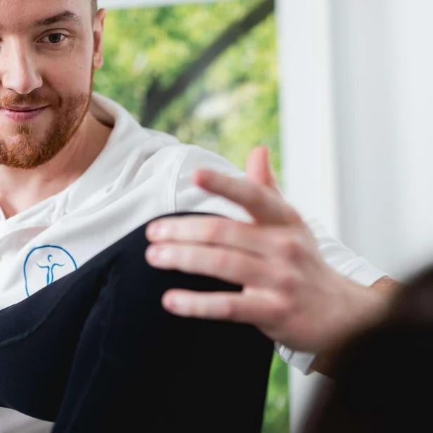 Christian Mahr lächelt einen Patienten an und erklärt eine Übung.