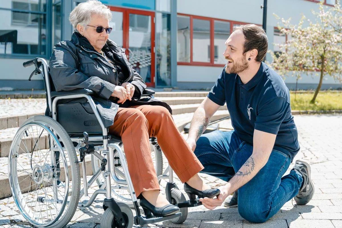 Ergotherapeut der Johannesbad Akademie hilft Seniorin im Rollstuhl