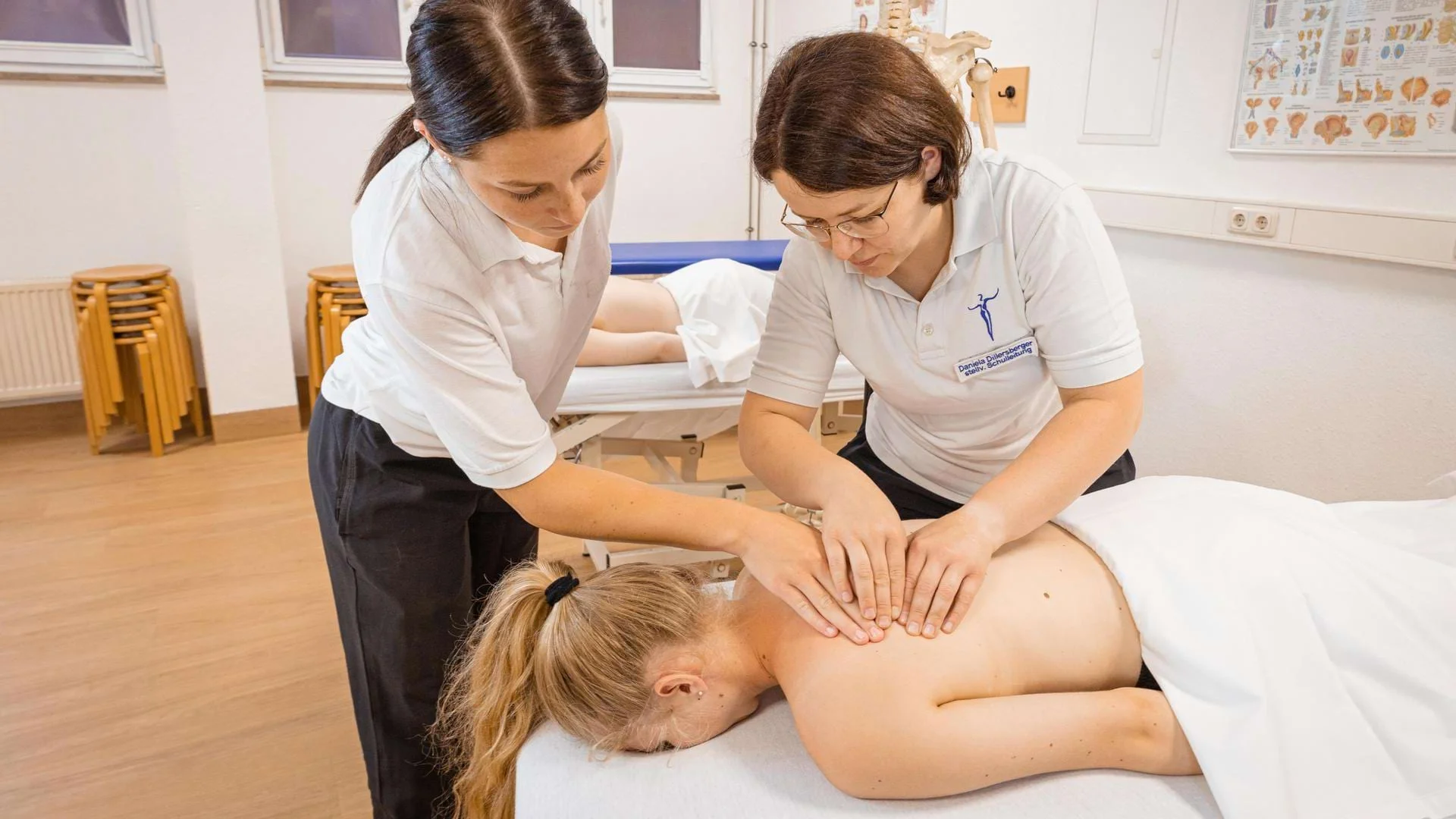 Lehrerin zeigt Schülern eine Rückenmassage in der Ausbildung zum Masseur und medizinischen Bademeister., Bild öffnen