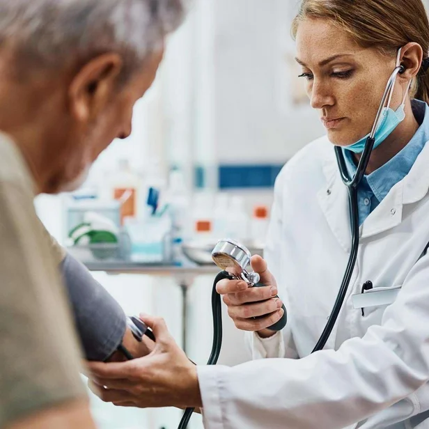 Ärztin für Allgemeinmedizin misst Blutdruck bei einem älteren Patienten.
