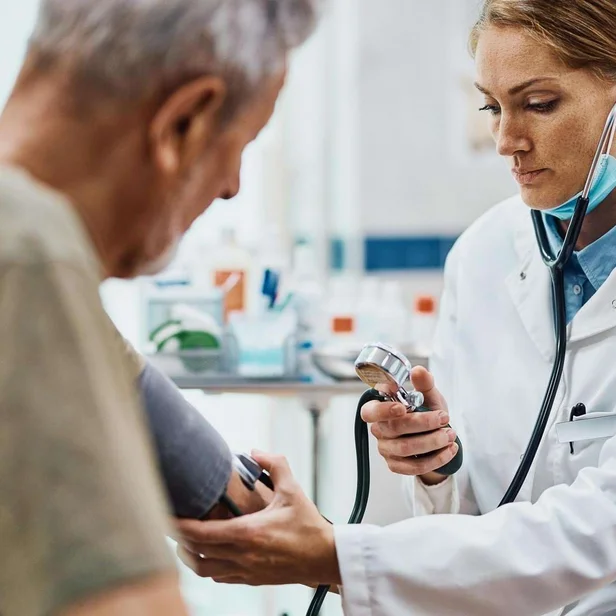 Ärztin für Allgemeinmedizin misst Blutdruck bei einem älteren Patienten.