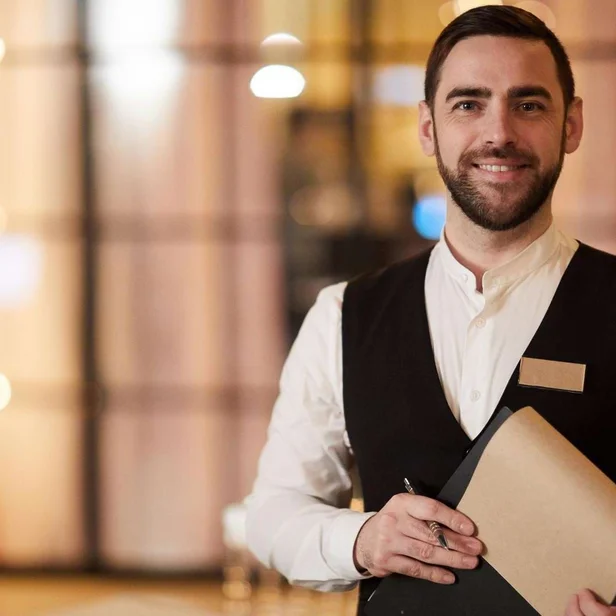 Restaurantleitung steht im Servicebereich und hält Unterlagen in der Hand.