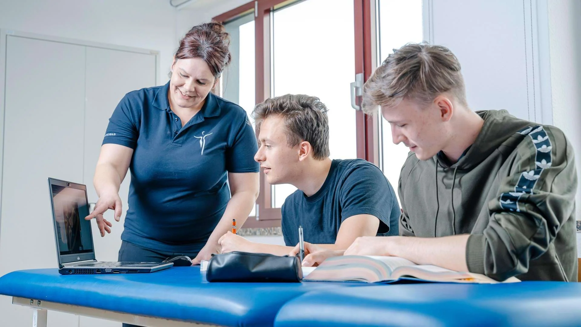 Dozentin bespricht mit Physiotherapie-Schülern Inhalte am Laptop. Auszubildende Physiotherapie im Unterricht