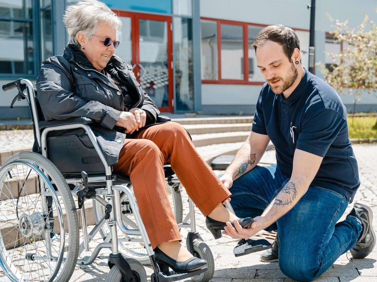 Ergotherapie-Schüler unterstützt eine Patientin im Rollstuhl. Ergotherapie-Schüler unterstützt eine Patientin im Rollstuhl.