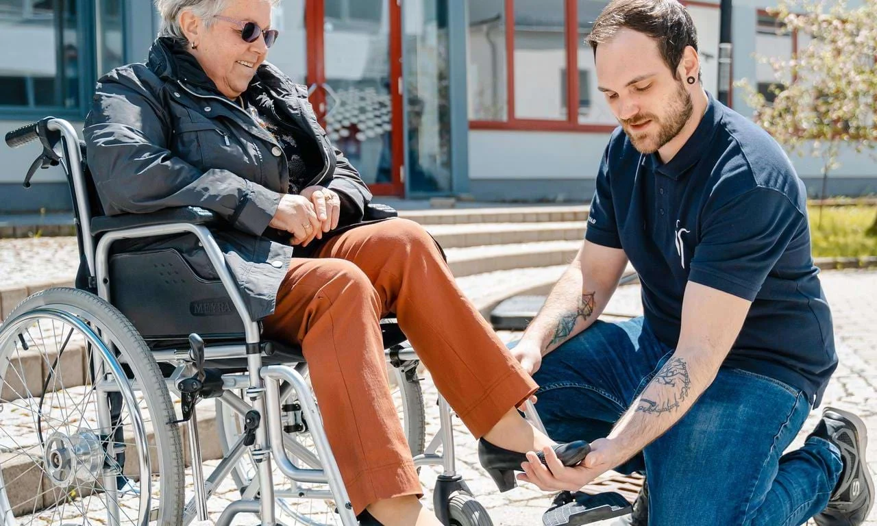 Ergotherapie-Schüler unterstützt eine Patientin im Rollstuhl. Ergotherapie-Schüler unterstützt eine Patientin im Rollstuhl.