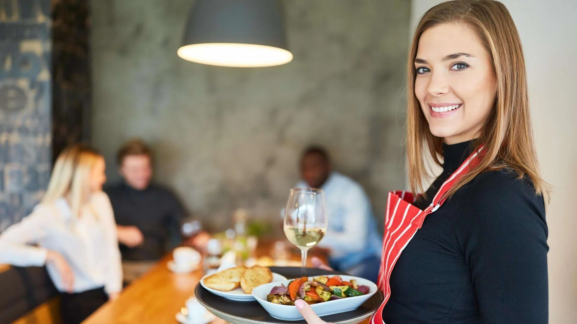 Eine Auszubildende zur Fachkraft für Gastronomie serviert Speisen im Restaurant., Bild öffnen