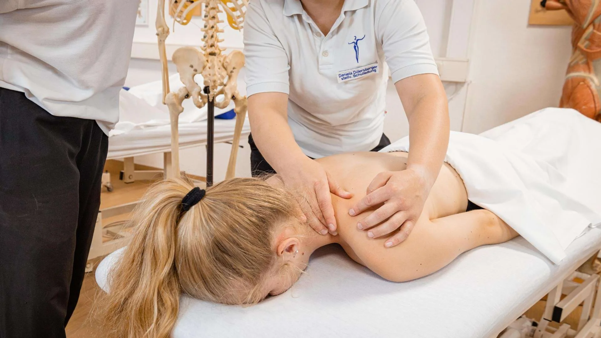 Lehrerin erklärt Schülern eine Rückenmassage in der Ausbildung zum Masseur und medizinischen Bademeister., Bild öffnen
